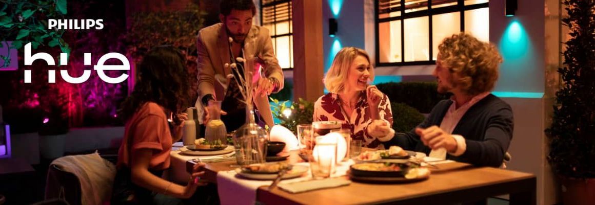 Mehrere Menschen sitzen an einem Tisch in einem mit Philips Hue ausgeleuchteten Wohnzimmer